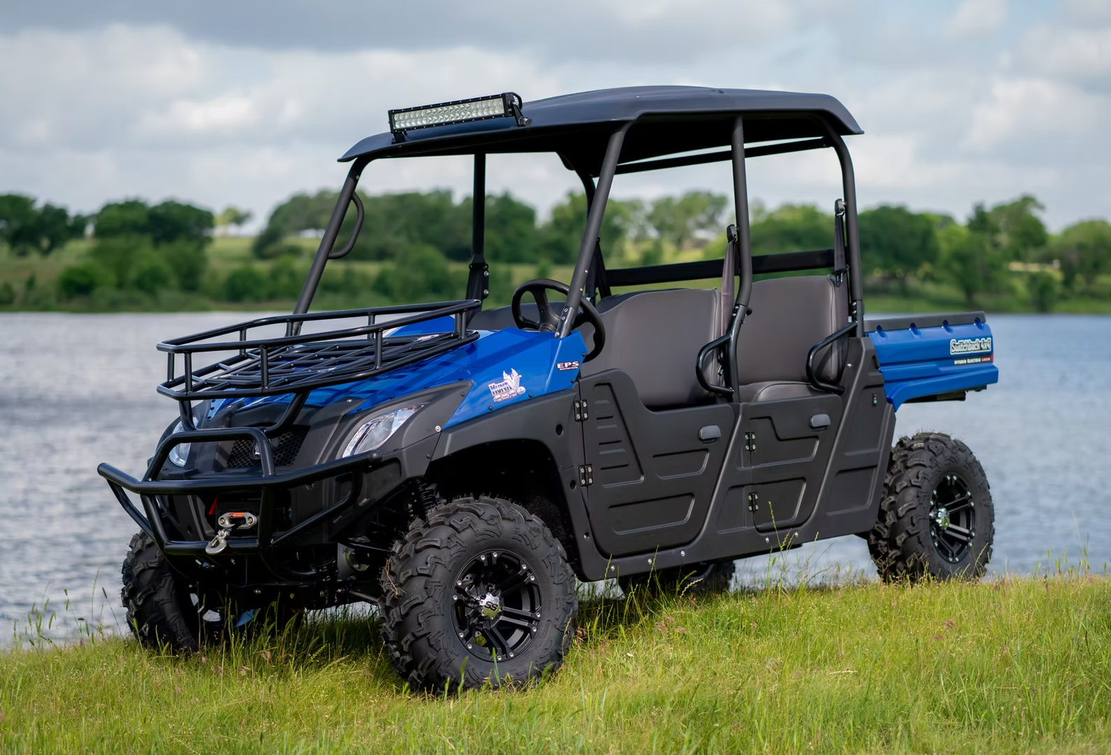 Blue crew cab utility vehicle with Double A-arm independent suspension for side by side parked by a lakeside trail.