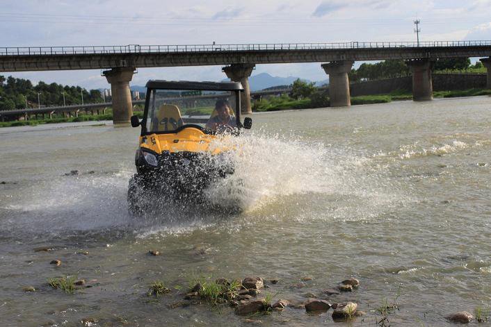 A 4WD UTV buggy wading through a rocky riverbed, demonstrating superior traction control and stability over slick stones.