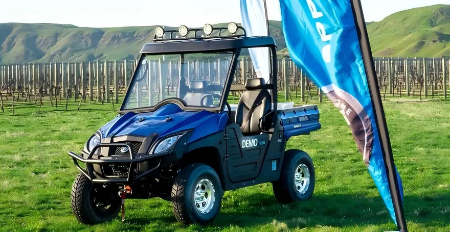 Off-road electric utility vehicle navigating uneven grass terrain and steep slopes