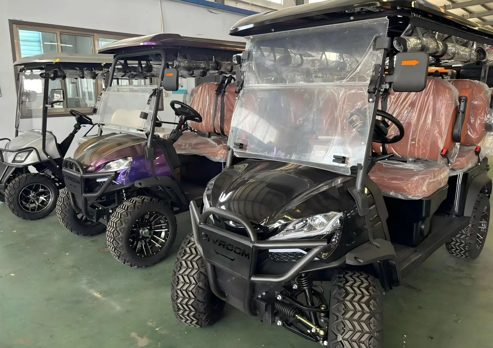A row of high-performance electric golf carts and 4-seater off-road utility vehicles ready for delivery in a factory warehouse.